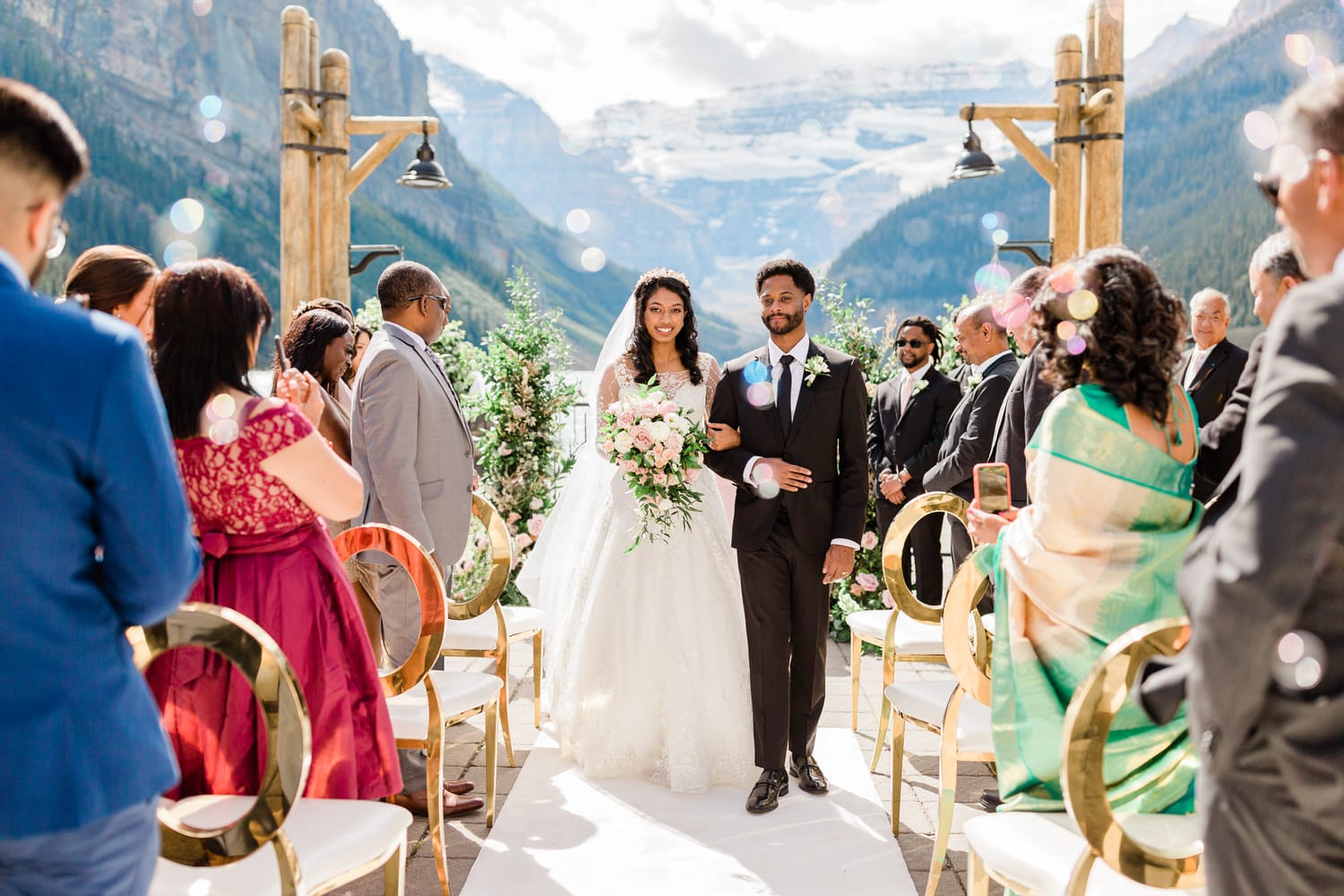 A bride and groom walking down the aisle during their outdoor wedding ceremony, surrounded by guests and stunning mountain scenery.