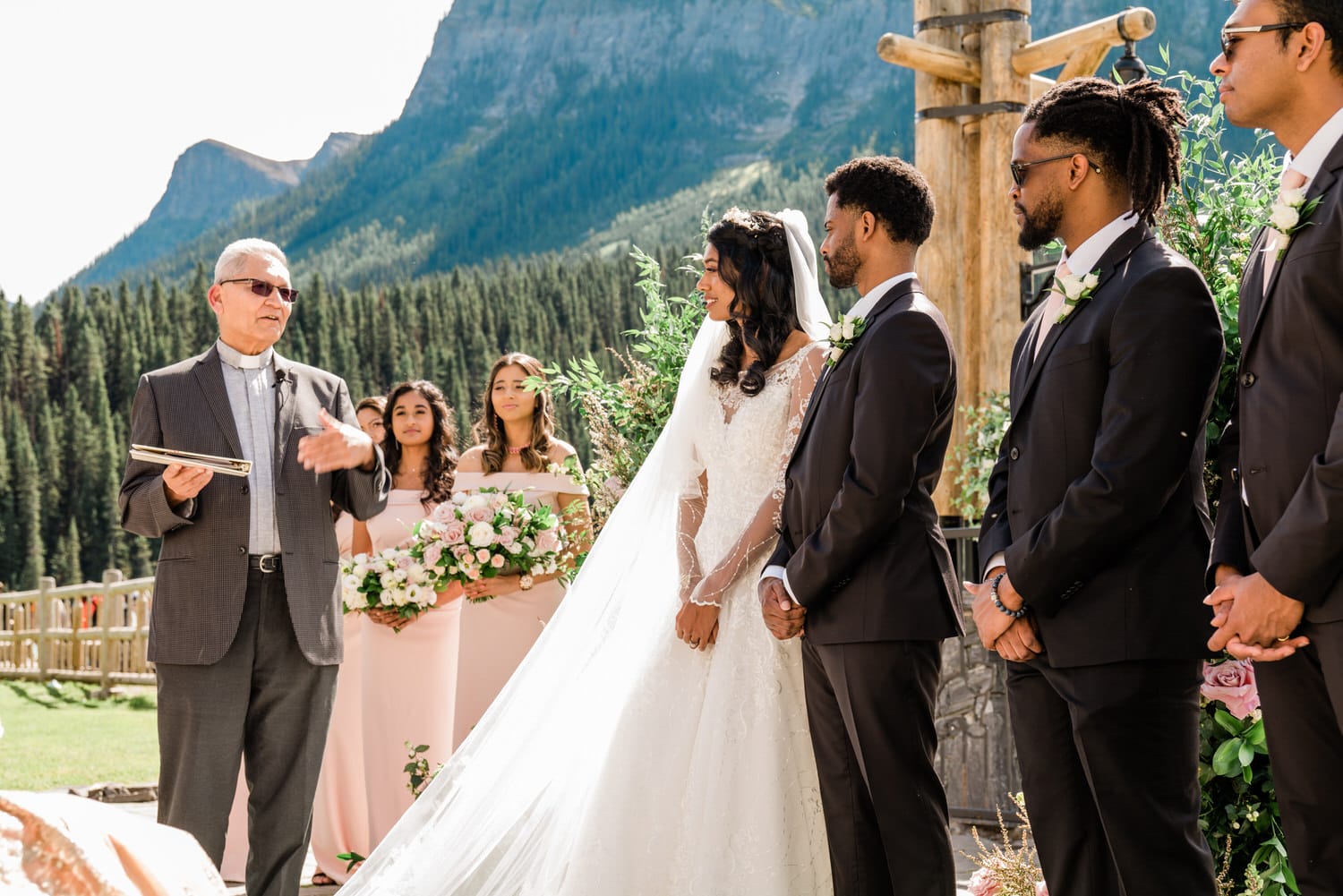 A beautiful outdoor wedding ceremony with a couple standing before an officiant, surrounded by bridesmaids, groomsmen, and a stunning mountain backdrop.