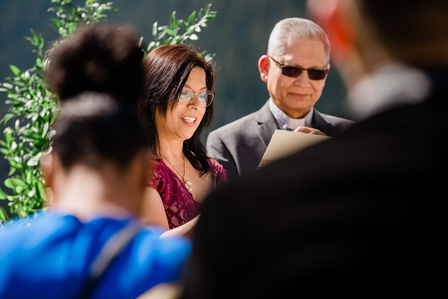 Ceremony Moment::A woman reads during a ceremony, surrounded by guests while an older man listens attentively.