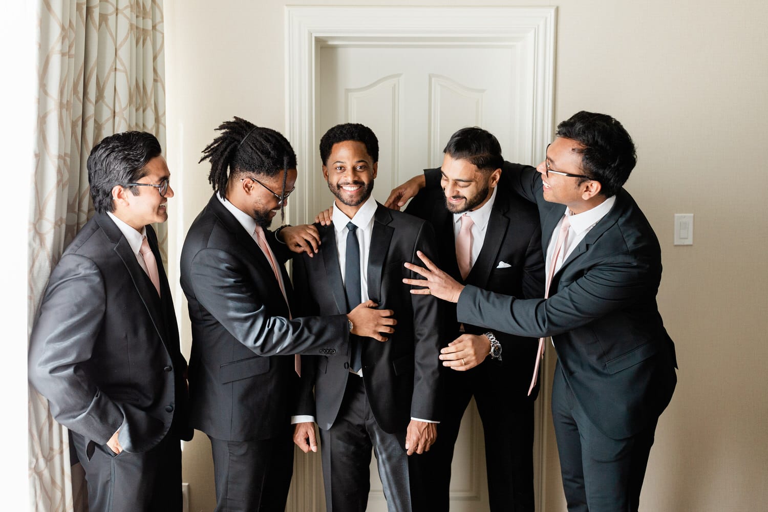 A joyful group of groomsmen adjusting suits and sharing laughter in a bright room, capturing the excitement before the wedding ceremony.