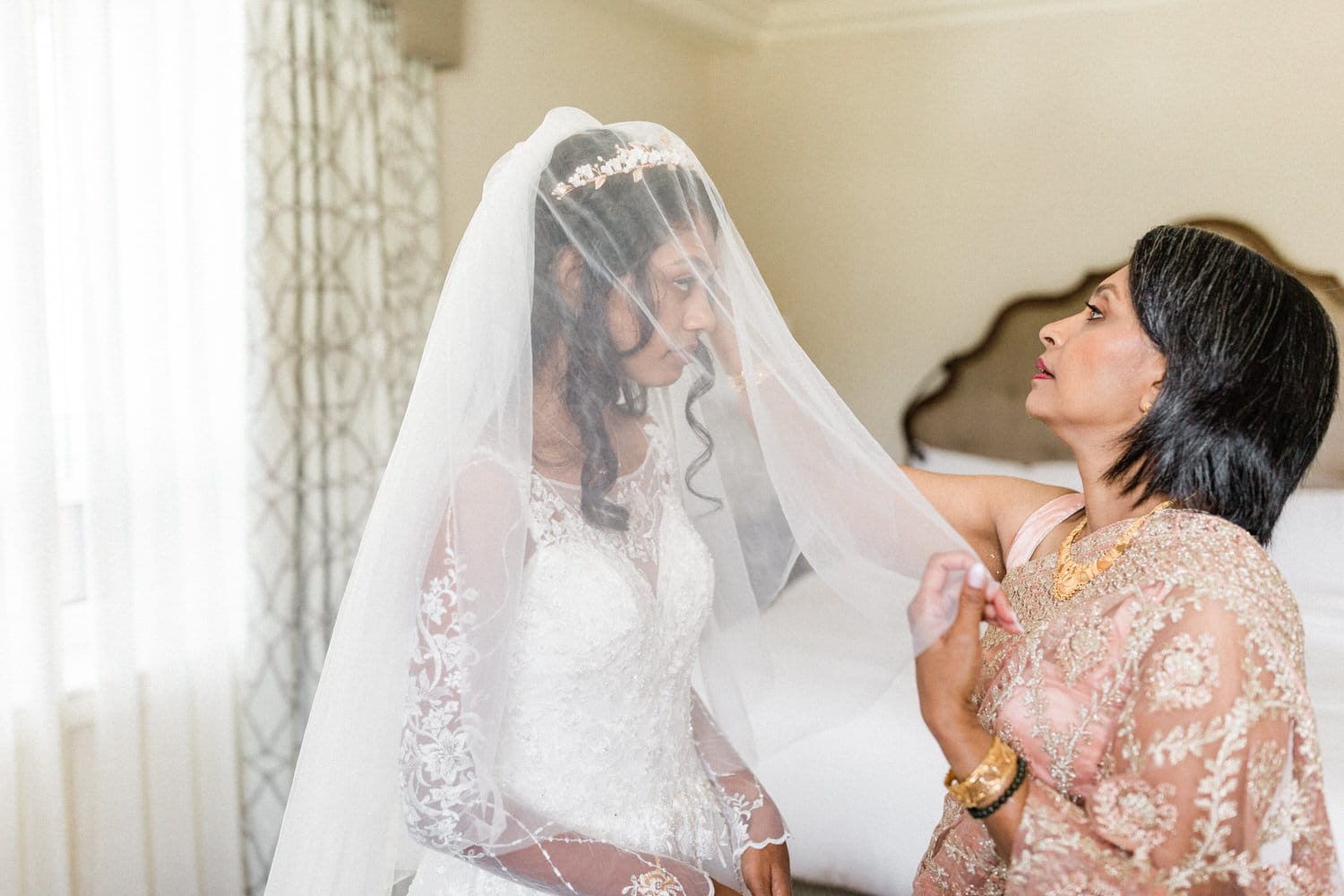 A bride being helped with her veil by her mother, capturing a heartfelt moment of preparation before the wedding ceremony.