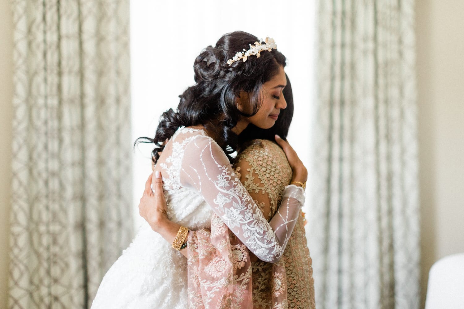 Two bridesmaids sharing a heartfelt embrace in a softly lit room, showcasing elegant attire and deep affection.