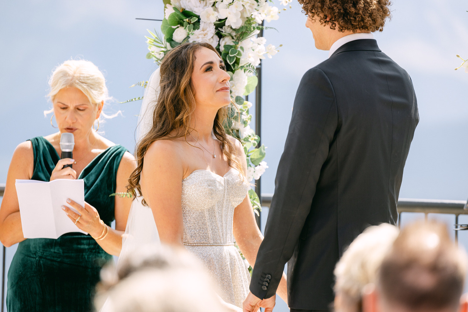 A bride gazes at her partner during a heartfelt moment in a wedding ceremony, while the officiant reads from a script.