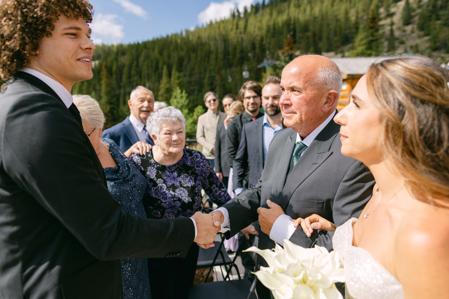 A joyful exchange between guests at a wedding ceremony, surrounded by nature and family.