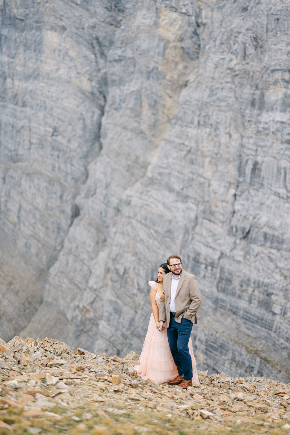 A couple embraces amidst a rocky mountain backdrop, showcasing a blend of elegance and nature.