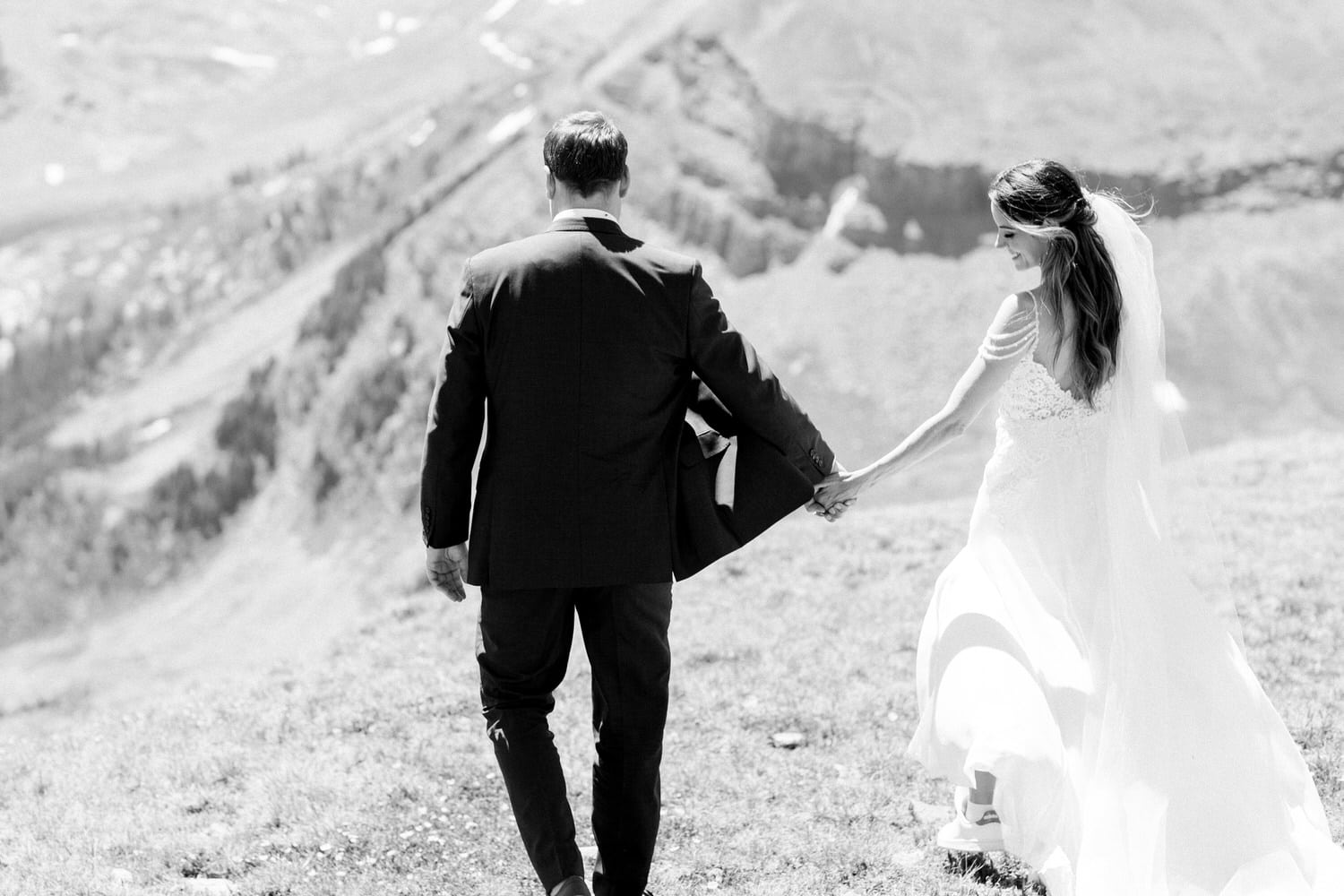 A couple walks hand in hand across a scenic landscape, celebrating their love against a backdrop of mountains.