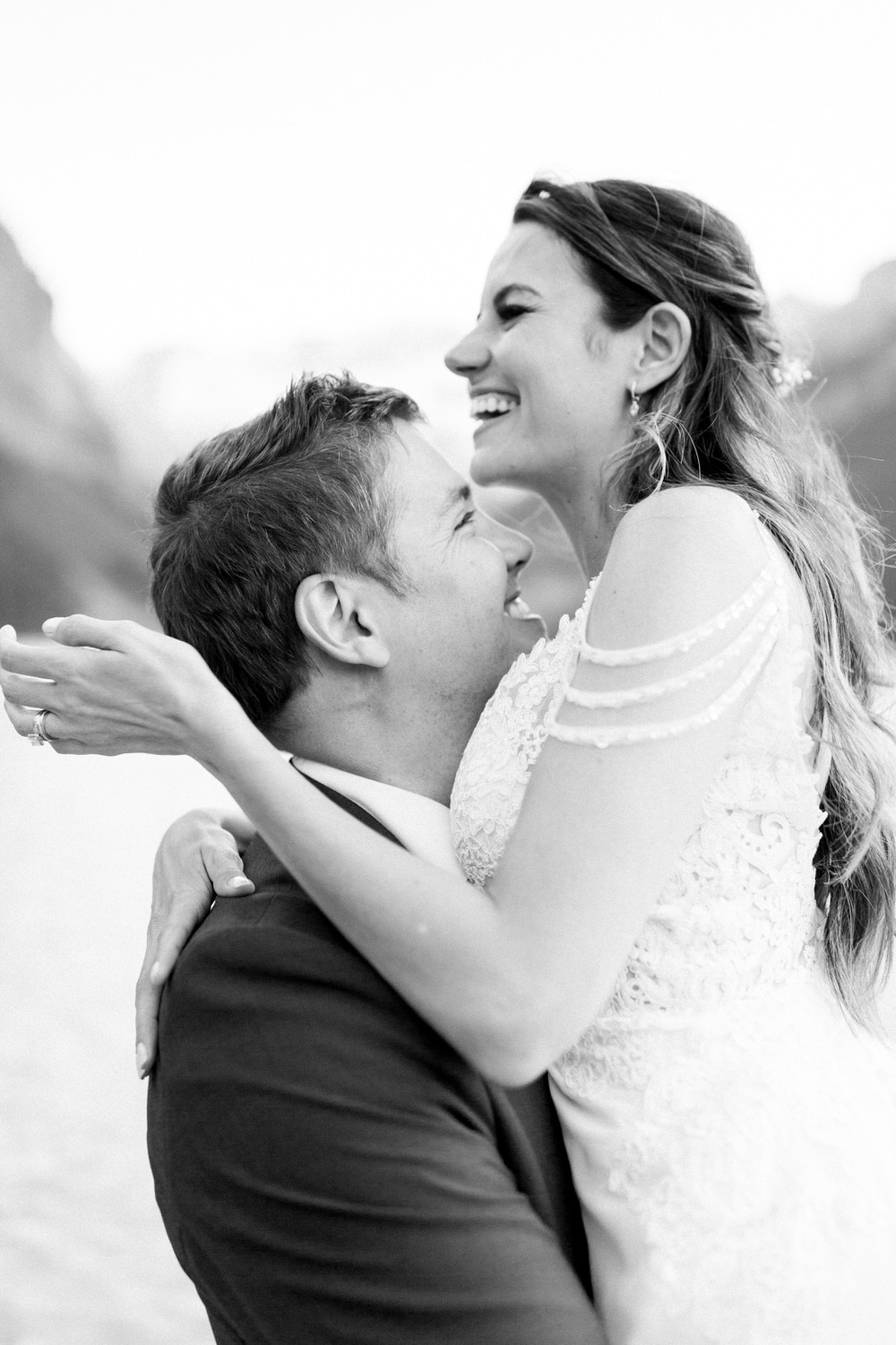 A couple embracing with joy, the bride smiling brightly as she holds the groom lovingly, set against a scenic backdrop.