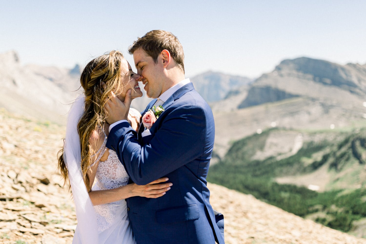 A bride and groom share a tender moment outdoors, surrounded by stunning mountain scenery, capturing their love in a natural setting.