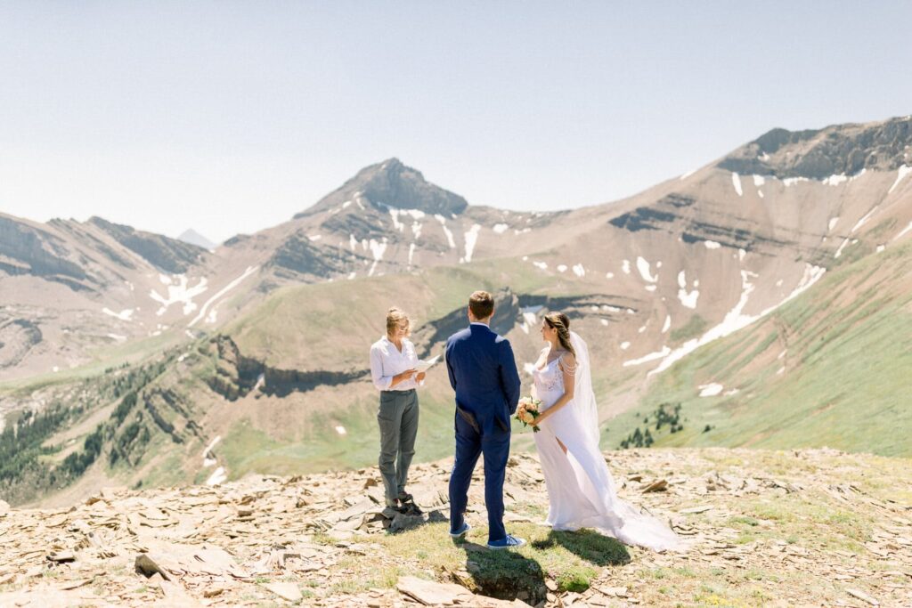 A couple exchanges vows during an outdoor wedding ceremony with majestic mountains as a backdrop.