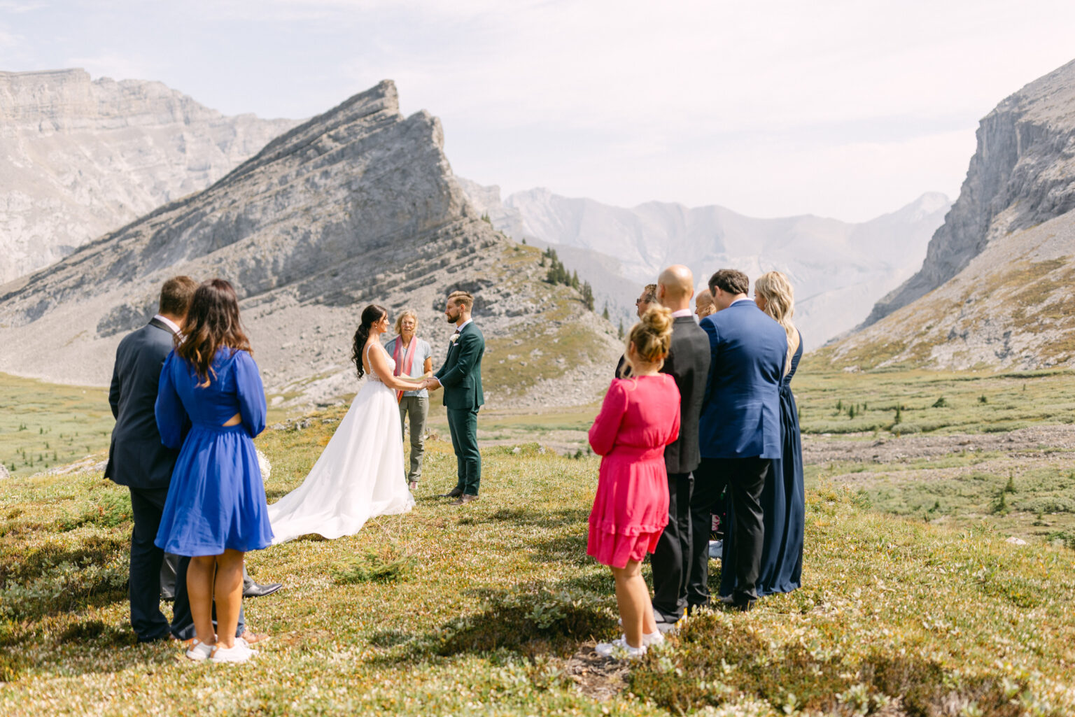 A couple exchanges vows during an outdoor wedding ceremony surrounded by guests in a picturesque mountainous setting.