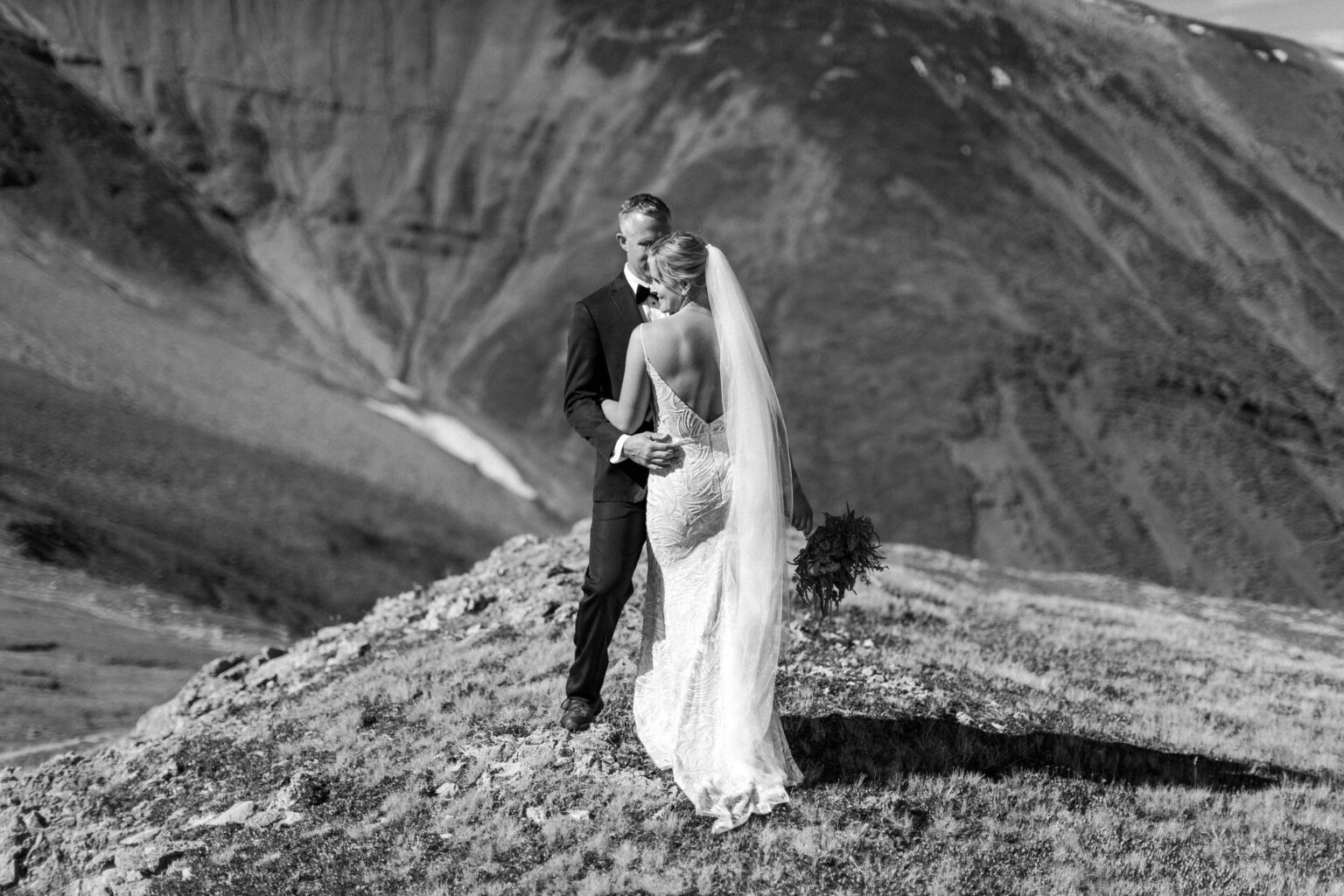 Bride and groom sharing a tender moment in a stunning mountainous landscape, dressed elegantly for their wedding.